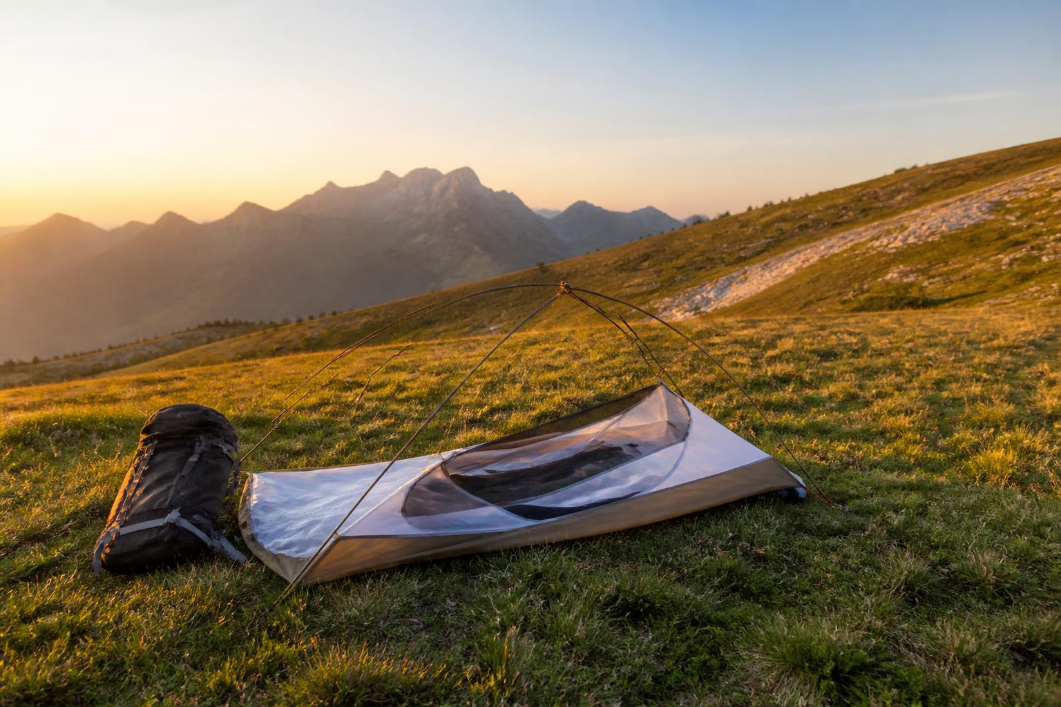 Installation tente bivouac en montagne sur prairie heure dorée