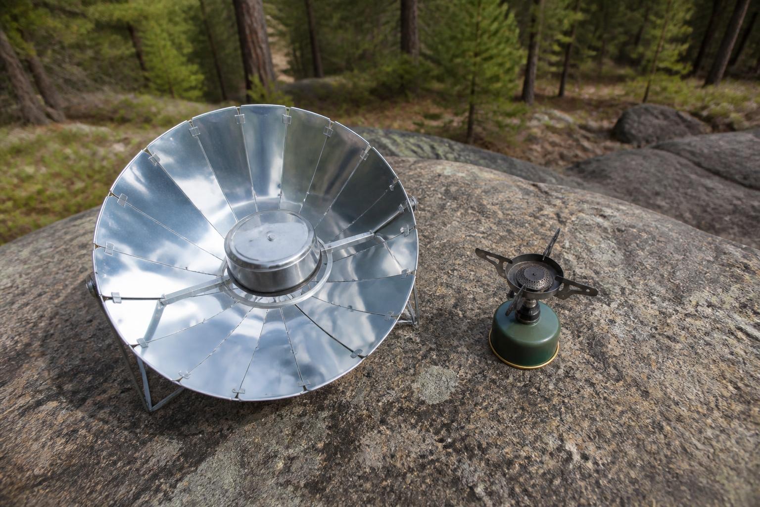 Barbecue solaire posé à côté d'un réchaud à gaz dans un campement en forêt