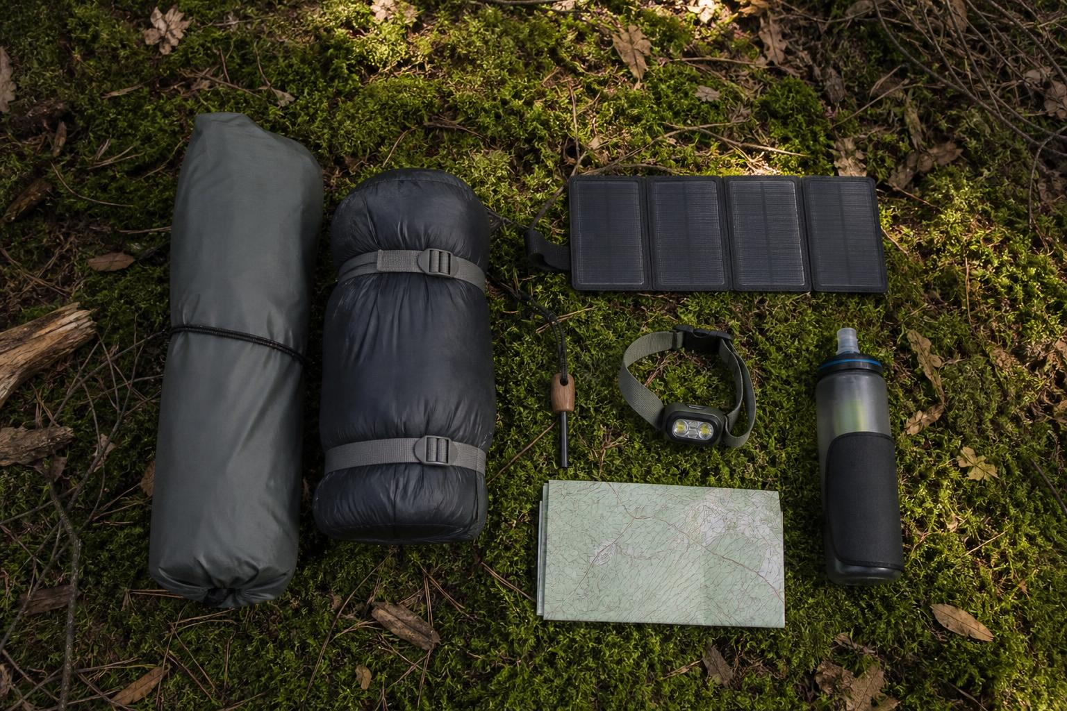 Matériel bivouac flatlay tente légère sac couchage batterie solaire kit survie forêt