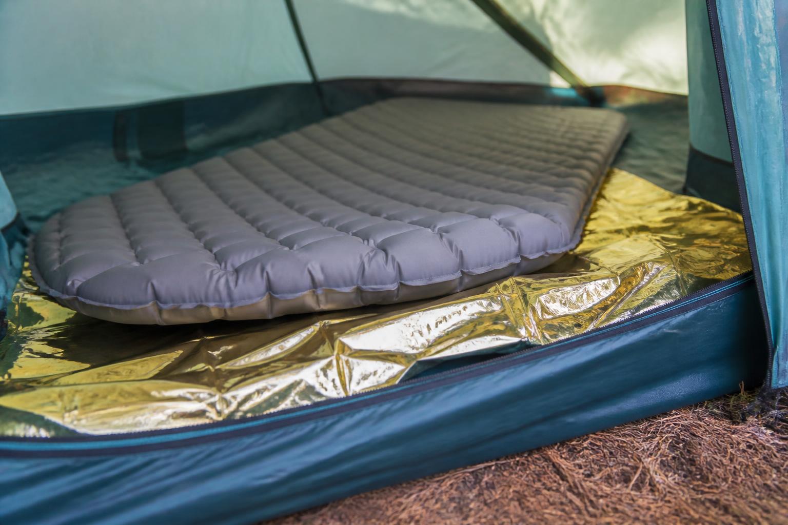 Couverture de survie dorée glissée sous matelas camping isolation sol
