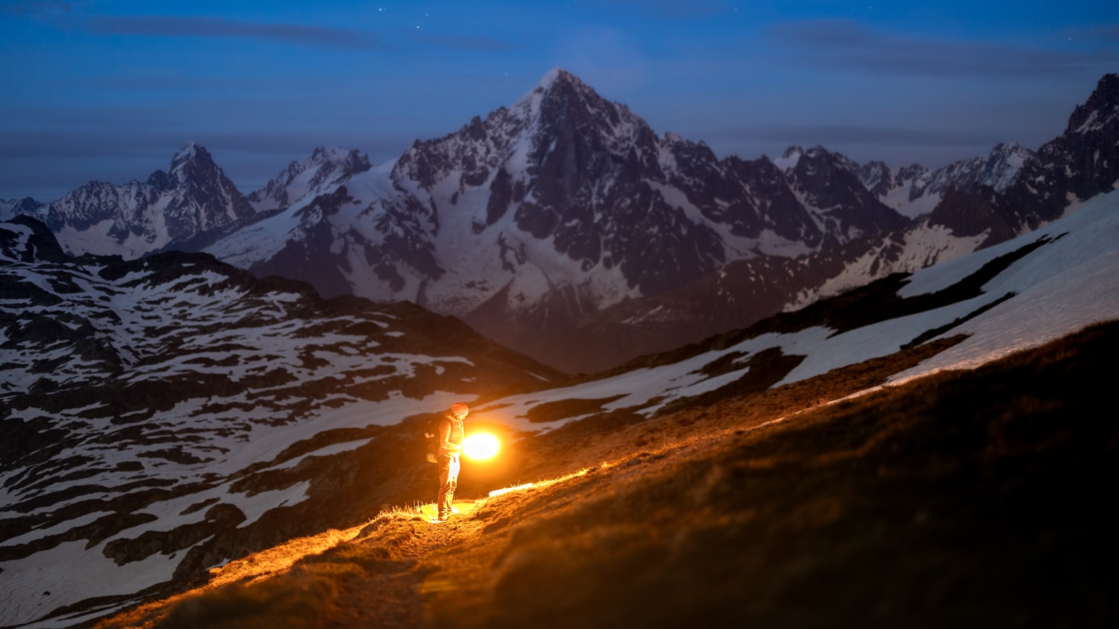 Randonneur équipé d'une lampe frontale LED sur un sentier de montagne enneigé la nuit